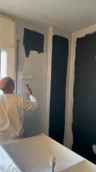 Pintor dando la capa de acabado blanca sobre la pintura apantallante negra en un dormitorio