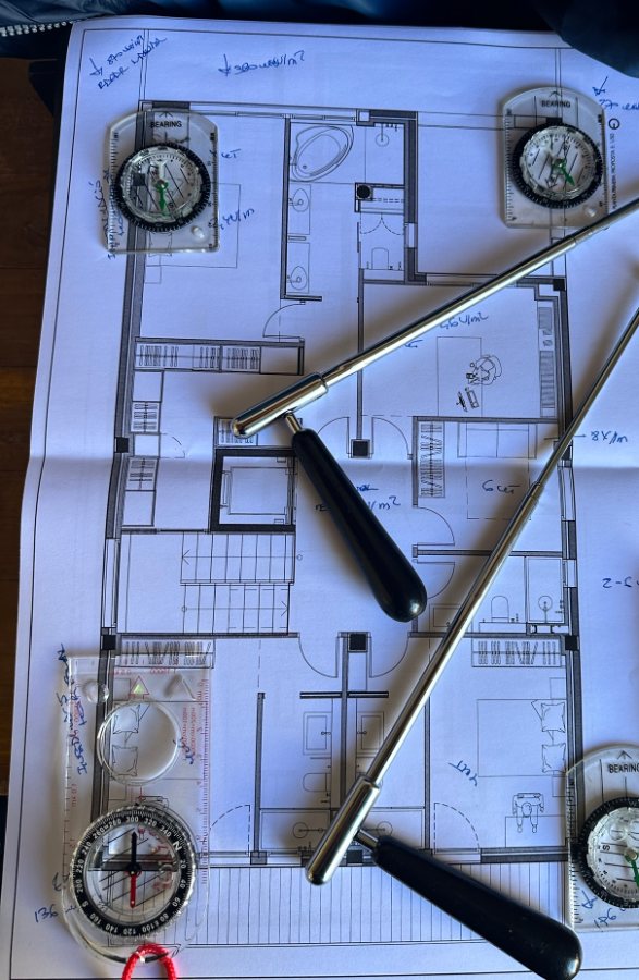 Prospección geobiológica sobre el plano de una vivienda con varillas y brújulas